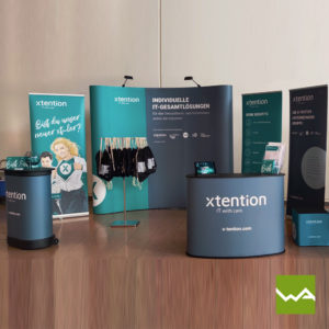 Messestand für das IT Unternehmen XTension bestehnd aus zwei Roll ups, einer Messwand Magnetic, einem Lamellen Counter Large und einem Werbeträger Sitzwürfel